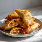 A pile of golden brown, crispy fried rice paper dumplings, one cut open to show vegetable filling.