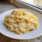 A serving of fettuccine pasta generously coated in rich homemade alfredo sauce and topped with black pepper.