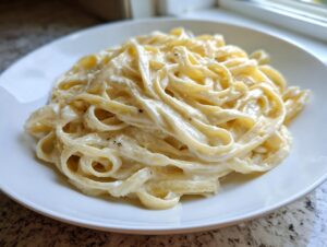 A close-up of fettuccine pasta generously coated in rich, creamy homemade alfredo sauce on a white plate.