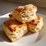 Close-up of three fluffy, square buttermilk biscuits stacked on a white plate, showing flaky layers.
