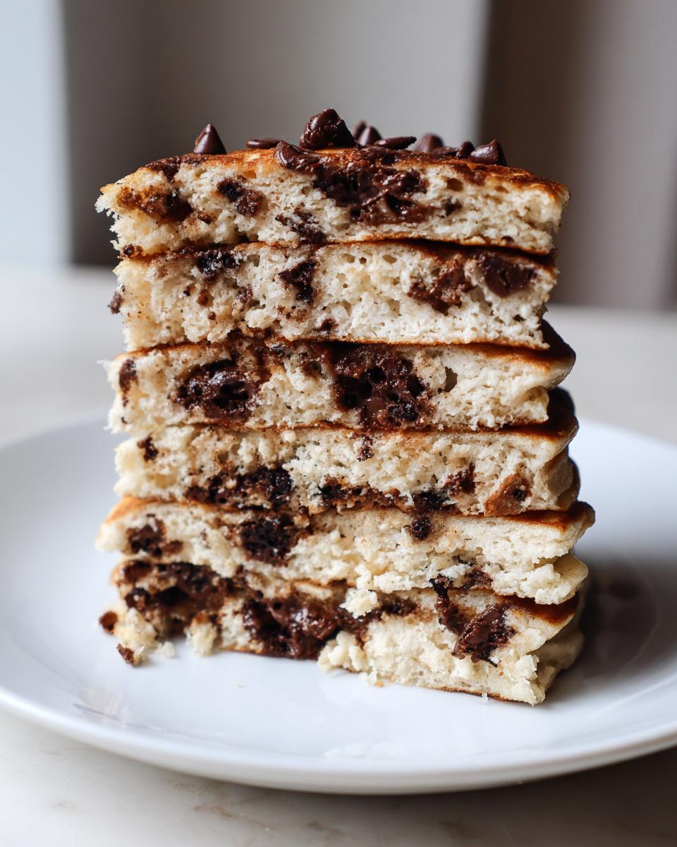 Close-up of a tall stack of fluffy chocolate chip pancakes showing melted chocolate inside.