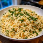 Close-up of a white bowl filled with fluffy rice pilaf mixed with toasted vermicelli and garnished with chopped parsley.