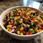 Close-up of colorful cowboy caviar featuring black beans, corn, red onion, and tomatoes.