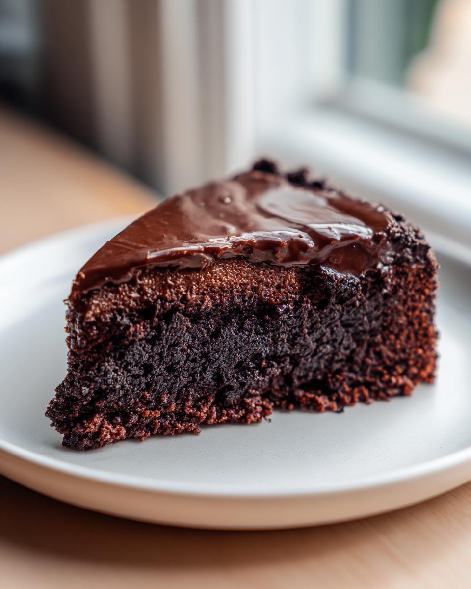 Close-up of a rich, fudgy slice of flourless chocolate cake topped with glossy chocolate ganache.