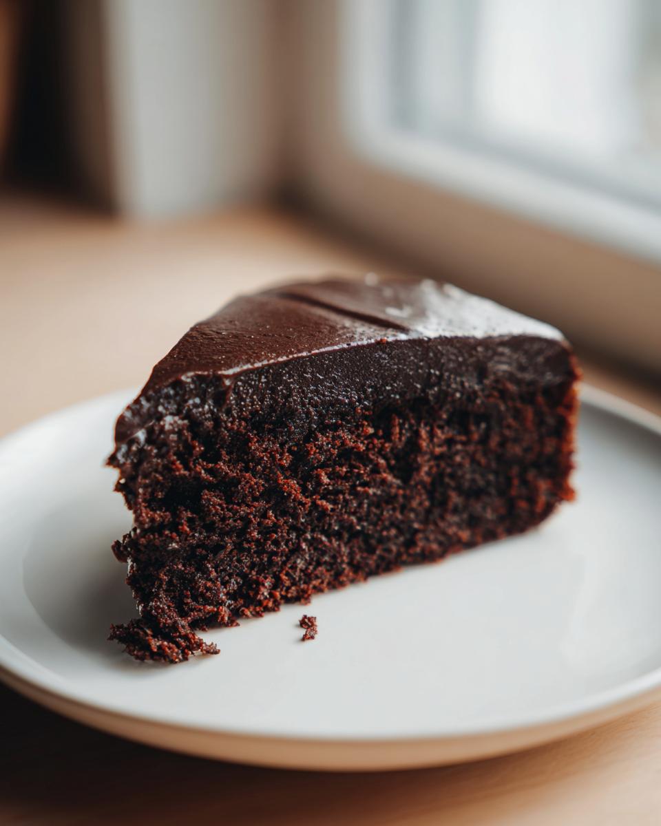 A rich, dark slice of fudgy flourless chocolate cake topped with smooth chocolate ganache on a white plate.