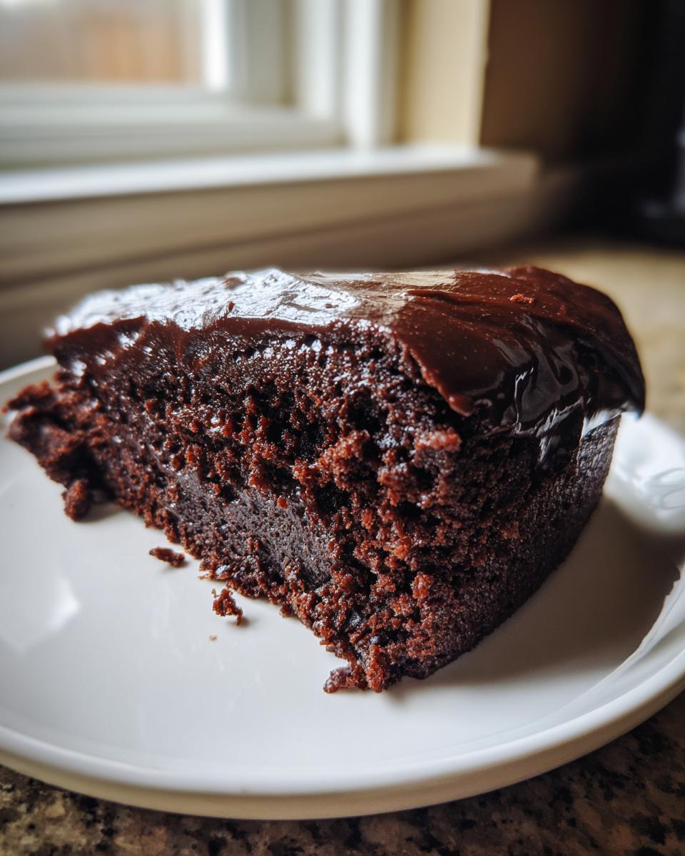 A close-up of a rich, fudgy slice of flourless chocolate cake topped with shiny chocolate ganache.