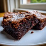 Close-up of fudgy gingerbread brownies dusted with powdered sugar on a white plate.