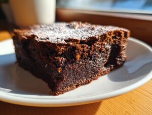 Close-up of a fudgy slice of gingerbread brownies dusted with powdered sugar on a white plate.
