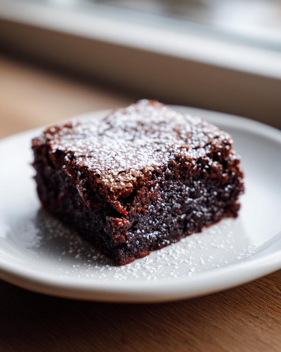 A close-up of a fudgy gingerbread brownies square dusted with powdered sugar on a white plate.