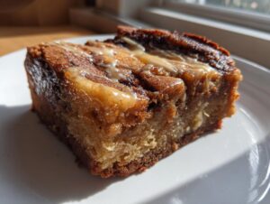 A close-up shot of a moist square of apple brownies topped with a light caramel or vanilla glaze.