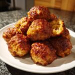 A pile of freshly baked, golden brown bisquick sausage balls stacked high on a white plate.