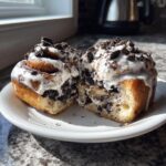 A gooey oreo cinnamon roll cut in half, showing the creamy filling and crushed cookie topping.