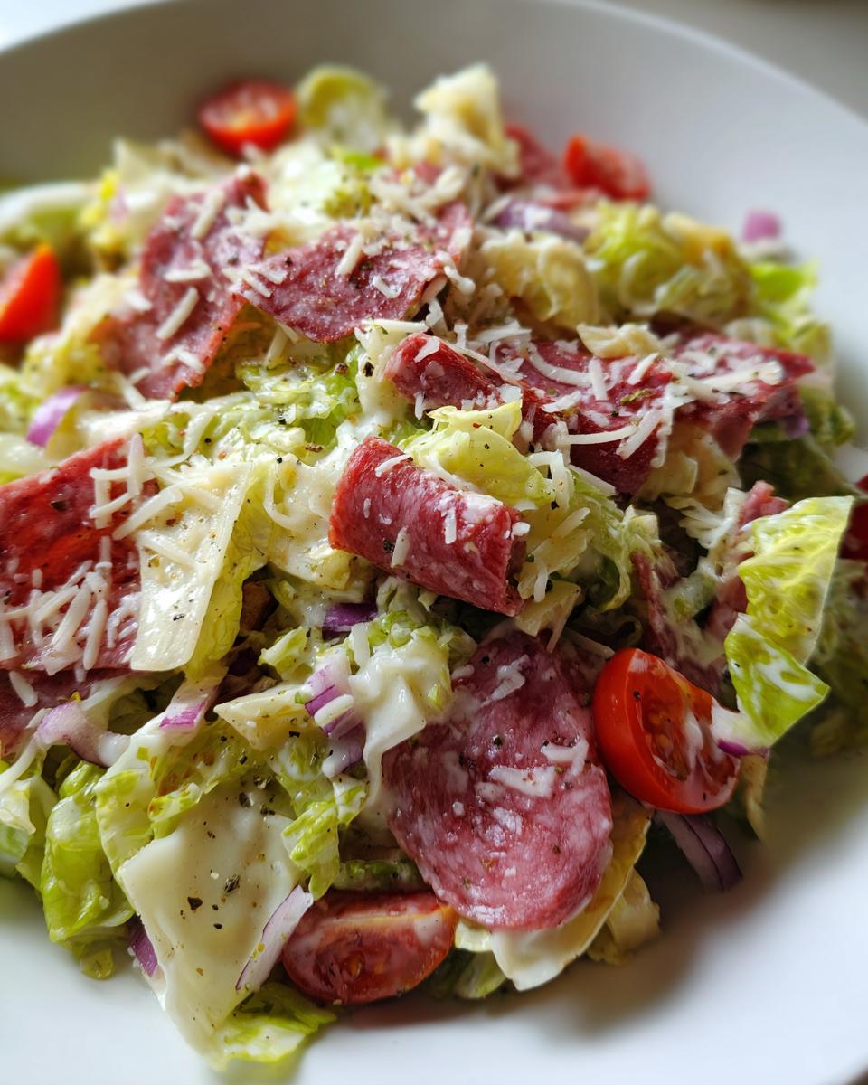 A close-up view of a vibrant grinder salad featuring lettuce, salami, cheese slices, red onion, and cherry tomatoes.