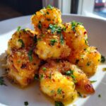 Close-up of golden, saucy Hawaiian garlic shrimp topped with fresh parsley and chili flakes.