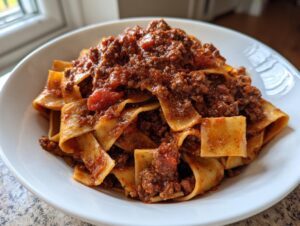 Close-up of wide pappardelle pasta generously topped with rich, hearty bolognese sauce in a white bowl.