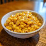 Close-up of a small white bowl filled with glazed, bright yellow honey butter corn.