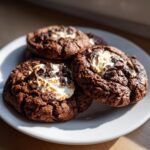 Close-up of rich, dark hot chocolate cookies topped with toasted marshmallow and chocolate chunks.