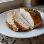 Two thick slices of juicy crockpot turkey breast seasoned with herbs on a white plate.