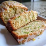Two slices of moist lemon zucchini bread, drizzled with a thick white glaze and showing flecks of green zucchini.