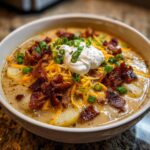 Close-up of a rich potato soup recipe topped with bacon, shredded cheese, sour cream, and green onions.