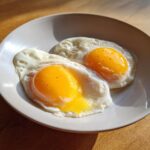 Two sunny-side-up style eggs, featuring bright yellow runny yolks, served on a light plate. These are the result of learning how to make perfect poached eggs.