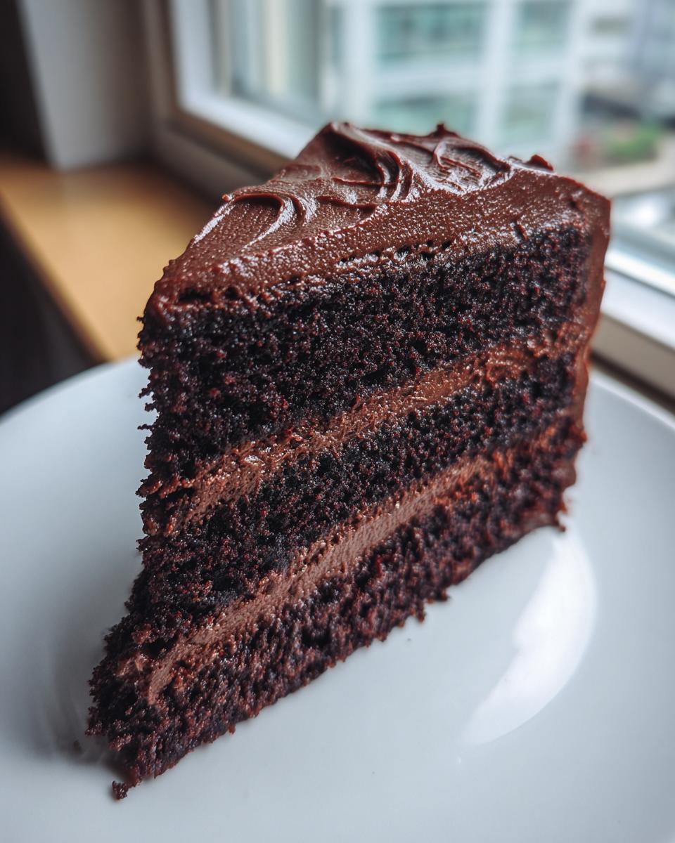 Close-up of a tall slice of moist chocolate cake with dark chocolate frosting layers.