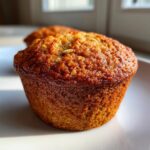 Close-up of a perfectly baked, golden brown oatmeal muffin sitting on a white plate.