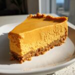 A perfect slice of rich, orange no bake pumpkin pie showing its creamy filling and crumbly crust on a white plate.
