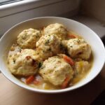 Close-up of a white bowl filled with creamy chicken and dumpling stew, topped with fresh parsley.