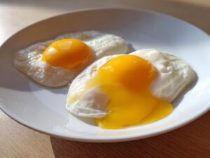 Two perfectly cooked poached eggs on a white plate, one with a runny yolk spilling out.
