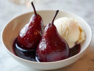 Two glossy, deep red poached pears served in a white bowl next to a scoop of vanilla ice cream.