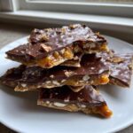 A stack of broken pieces of saltine cracker toffee showing the caramel, cracker, and chocolate layers topped with nuts.