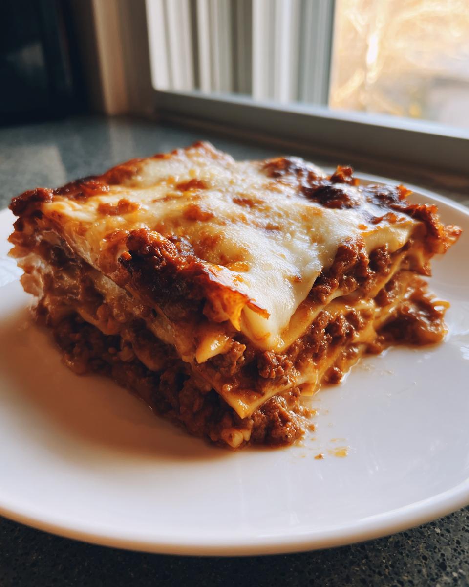 A thick, layered slice of sheet pan lasagna with rich meat sauce and melted, browned cheese topping.