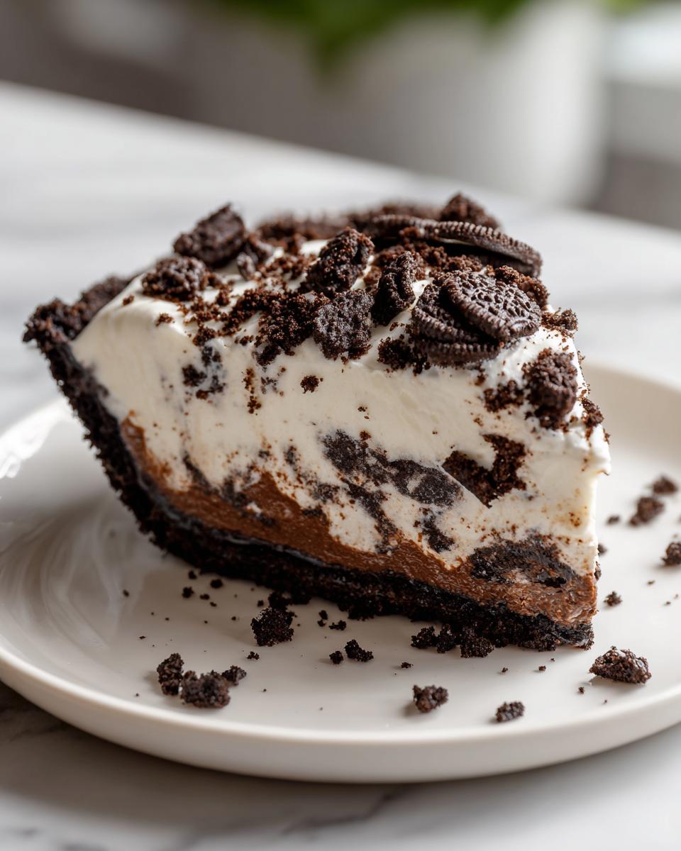 A generous slice of creamy, layered oreo pie topped with crushed cookies on a white plate.