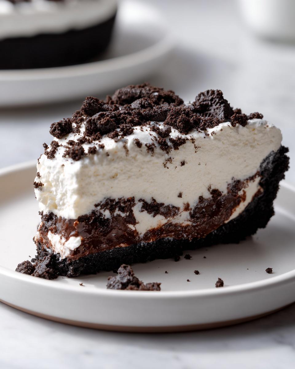 A thick slice of rich oreo pie with a dark crust, chocolate layer, and white whipped topping, sprinkled with cookie crumbs.