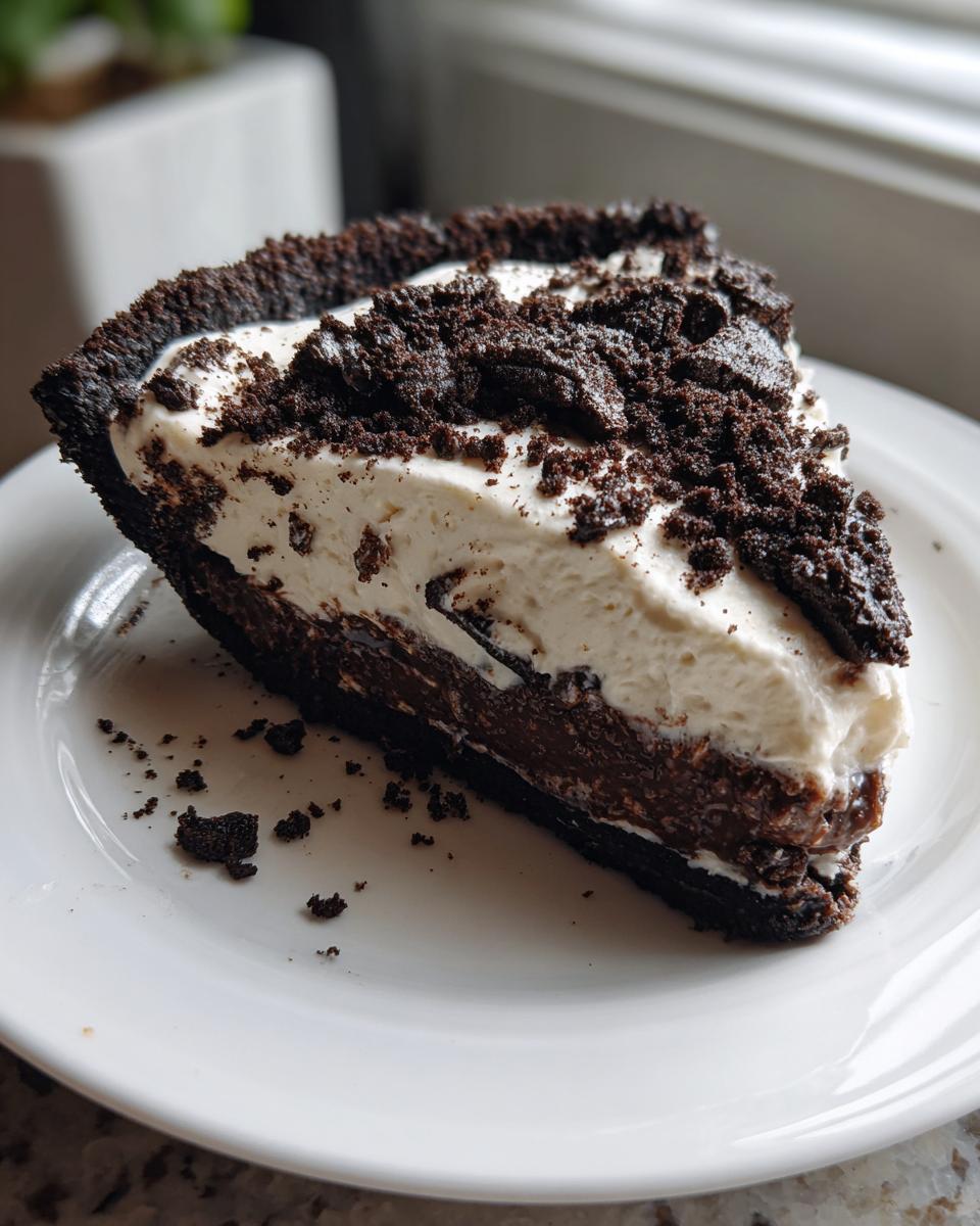 A decadent slice of no-bake oreo pie featuring a dark chocolate crust, rich filling, and whipped topping sprinkled with crumbs.