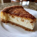 A close-up of a creamy slice of snickerdoodle cheesecake with a thick graham cracker crust and a heavy cinnamon-sugar topping.