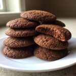 A stack of dark brown, chewy soft gingerbread cookies, one broken open to show the texture.