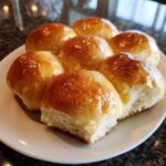 A cluster of six golden-brown, glossy sourdough discard rolls served on a white plate.