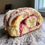 Close-up of a Strawberry Cheesecake Sweet Rolls cross-section showing fluffy dough, bright red filling, and white icing drizzle.