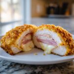 Close-up of a crispy, golden-brown chicken cordon bleu cut in half, showing melted cheese oozing out.