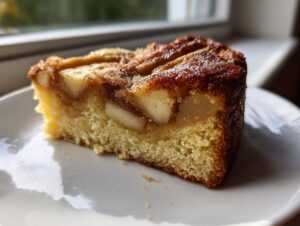 Close-up of a moist slice of swedish apple cake showing tender cake base and baked apple pieces on top.