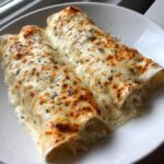 Two delicious white chicken enchiladas covered in melted, bubbly white cheese and sprinkled with herbs.