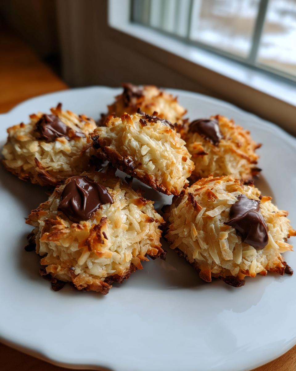 A close-up of several golden brown almond joy cookies topped with melted chocolate, resting on a white plate.