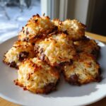 A stack of freshly baked, golden brown almond joy cookies featuring toasted coconut and visible chocolate chips.