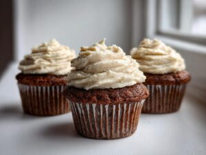 Three rich, dark gingerbread cupcakes topped with thick swirls of light-colored cream cheese frosting.