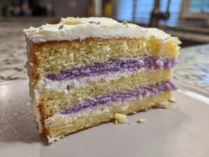 Close-up of a slice of amazing lavender cake with three layers of yellow sponge, purple filling, and white frosting.