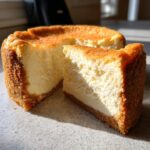 A whole new york cheesecake with one thick slice cut out, showing the creamy texture and graham cracker crust.