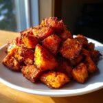 A mound of perfectly seasoned roasted sweet potatoes cubes piled high on a white plate.