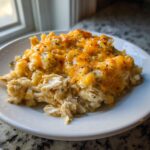A close-up serving of creamy chicken cauliflower rice casserole topped with melted cheddar cheese and herbs.